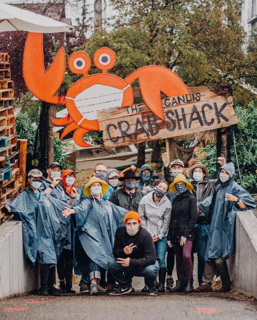 Canlis employees stand infront of a new Canlis sign advertising it as a Crab Shack