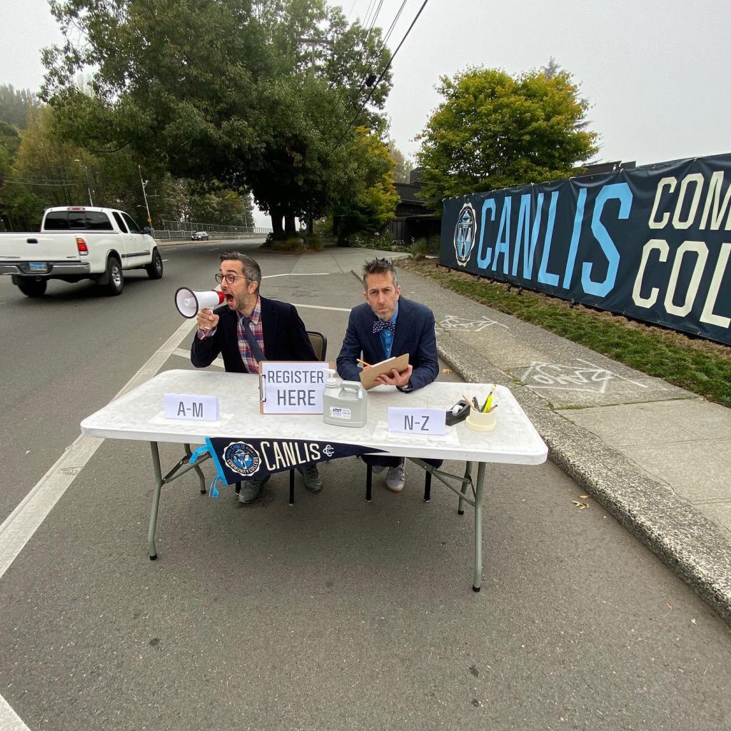 Mark and Brian Canlis sit at a table offering registration for food and beverage classes at the Canlis Community College.