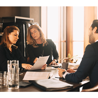 Two women review papers as a man looks at them from across the table