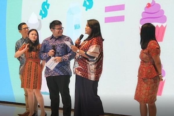 Three women and two men holding microphones standing in front of a colorful backdrop of large cupcakes.