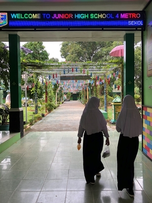 School entrance and walkway with two girls walking away under a sign that reads, “Welcome to Junior High School”