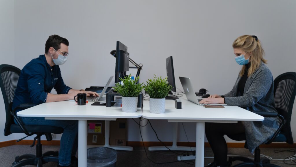 Image of employees wearing masks and social distancing in the workplace. Caption: Conflicting guidelines can make it confusing to ensure a safe working environment.