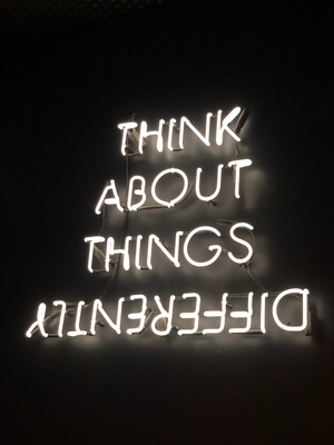 Neon sign with this text: “think about things differently” - "differently appears backwards