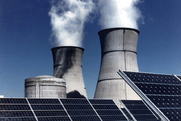 Solar panels with industrial smoke stacks behind them
