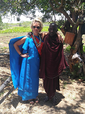 Anissa Buckley standing under a shady tree, arm-in-arm with a Maasai tribe member