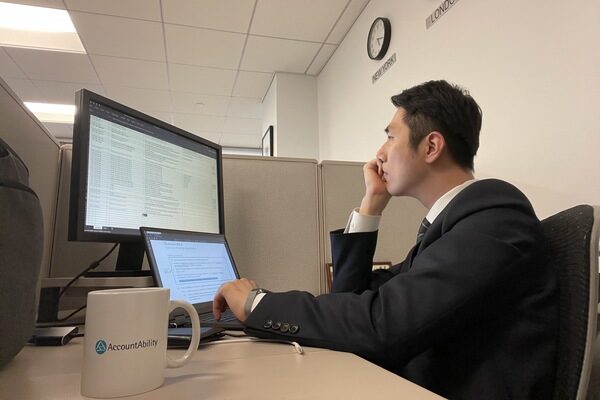 A picture of Duncan Lee working at his cubicle at the NYC office, with an AccountAbility mug.