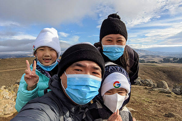 Chao Wang with his wife and their young daughters wearing masks and coats and hats outside with an arid, mountainous landscape and blue sky in the background 