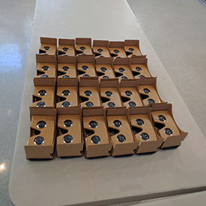 24 sets of Google Cardboard VR viewers laid out side by side on a table
