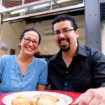 Mama Said Hand Pies owners Hiroko Takashima and Gabe Flores sitting at a table with a plate of hand pies in front of them and smiling