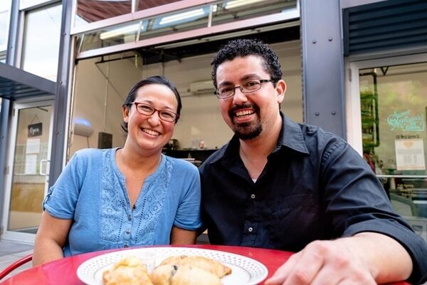 Mama Said Hand Pies owners Hiroko Takashima and Gabe Flores sitting at a table with a plate of hand pies in front of them and smiling