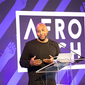 Marlon Nichols speaking at a podium with an Afro Tech sign in the background
