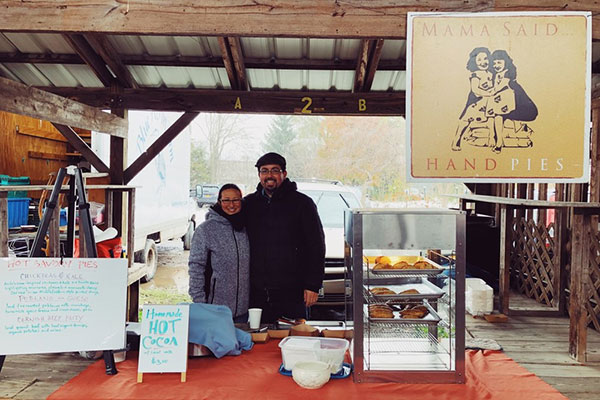 Hiroko Takashima and Gabe Flores in winter coats standing in their stall at the Ithaca Farmers Market