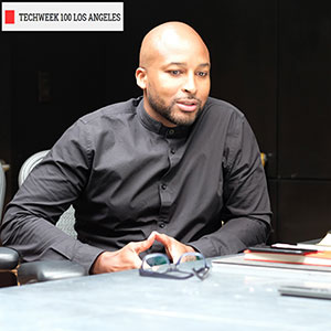 Marlon Nichols seated at a conference table with banner text overlaid on the upper left corner of the photo, "Techweek 100 Los Angeles"