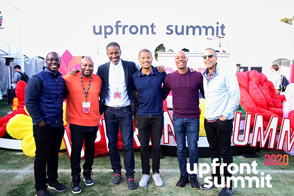 Marlon Nichols arm-in-arm with 5 other Black men standing below an Upfront Summit banner/sign