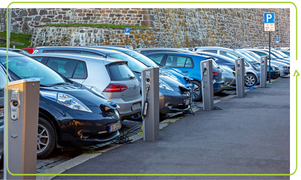 a line of cars parked on a street and plugged into charging stations with a stone wall in the background