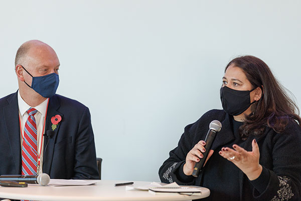 Andrew Karolyi and Momina Aijazuddin seated at a table; Momina is holding a mic and speaking