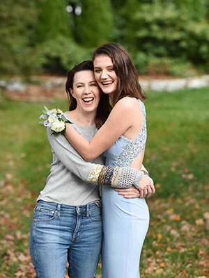 photo of Julie Belkus and her daughter standing and hugging each other, looking at the camera and smiling, with green grass and trees in the background