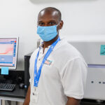 Pradeep Ambrose standing in a lab in front of lab equipment on a counter behind him