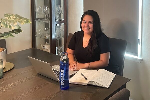 Natalie interning for Ecolab from home. In front of her is a table, laptop, notebook, and an Ecolab water bottle.