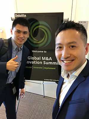 Steve Cheng in the foreground standing net to a sign that reads: Deloitte Global M&A Innovation Summit. A colleague stands on the other side of the sign with a thumbs up