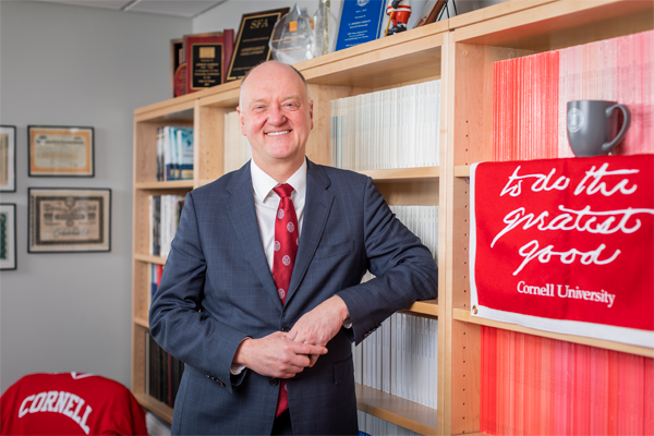 Upper body photo of Andrew Karolyi standing with his elbow on a bookshelf nest to a red banner hanging for a bookshelf in the foreground