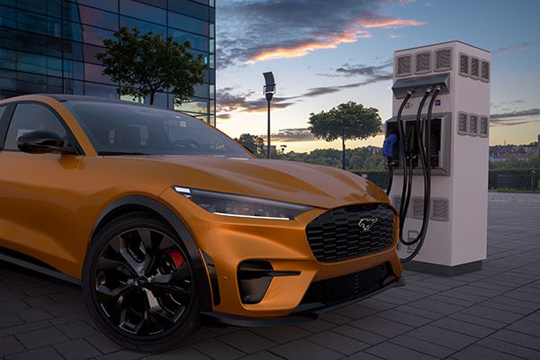 A picture of a mustard colored Ford Mustang electric vehicle sitting at an EV charging station.