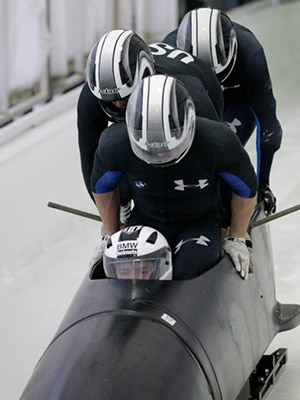 four men in helmets packed into a bobsled and pushing off