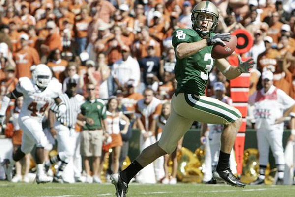 Thomas White in a football uniform and helmet running, looking behind him, and catching a footbal,l with bleachers filled with people in the background