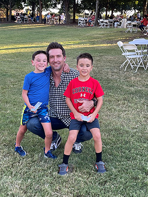 Thomas White squatting on the grass with his arms around a young boy on each knee