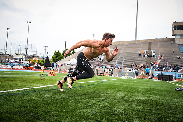 Thomas White racing, feet in midair, across a green with people on bleachers in the background