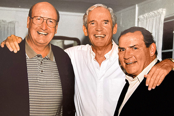 photo of 3 men with arms around each other, facing the camera and smiling
