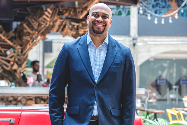 Lawrence Watkins in a suit smiling in front of a car
