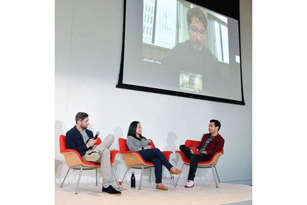 2 men and 1 woman seated in chairs on stage and 1 man and 1 woman on the screen, speaking remotely