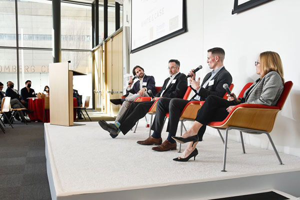 3 men and one woman sitting on chairs on a stage and speaking 