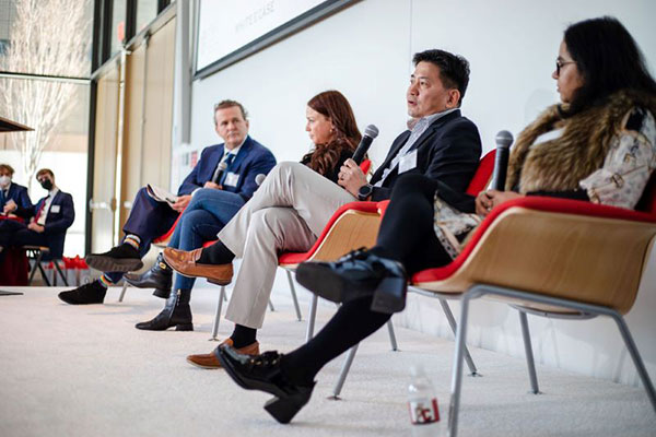 2 men and 3 women sitting on chairs on a stage and speaking