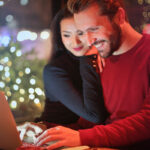 Couple standing together smiling while looking at a laptop