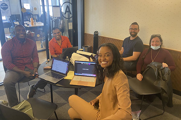 5 diverse adults sitting around a round table with laptops in a small conference room