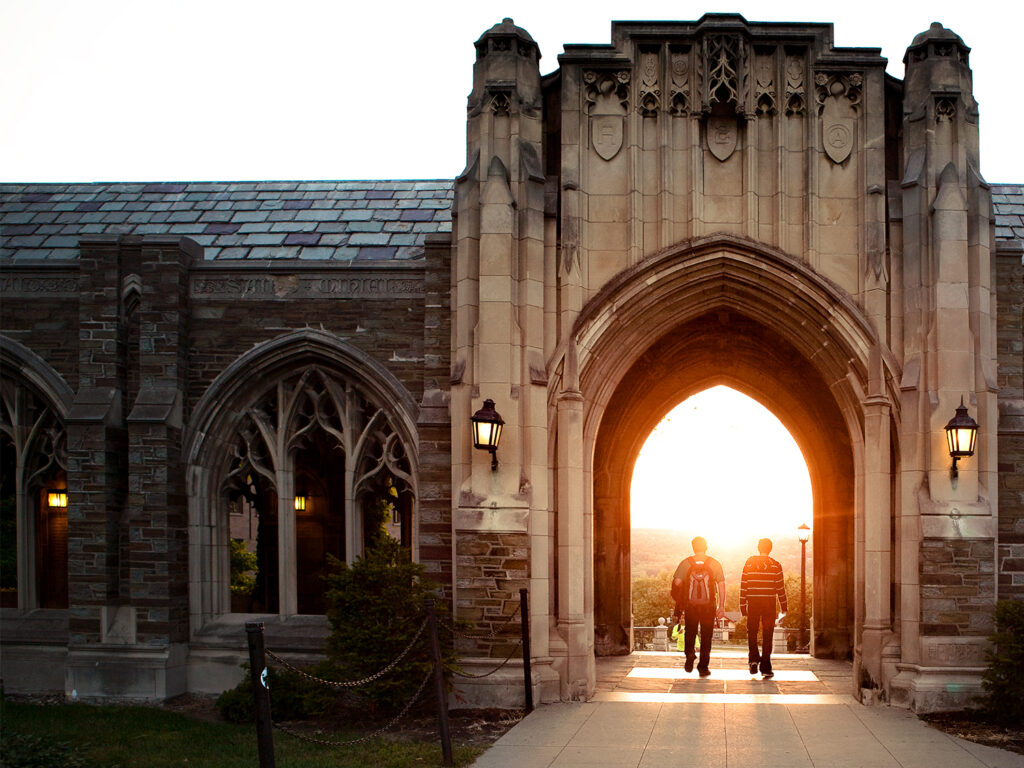 Two students walk through an archway into the sunset.