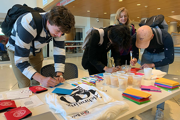 students with backpacks on leaning over a table and writing notes on colorful note paper