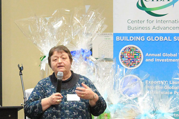 Elena Iankova holding a microphone and speaking next to a CIBA banner.