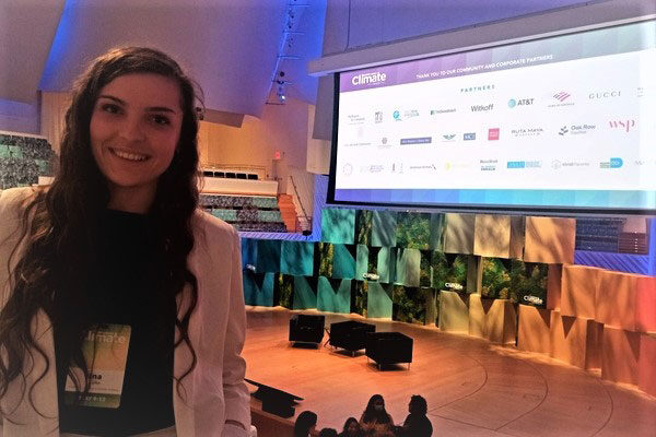 A picture of Ina Gjika at the opening plenary of the conference with the stage and big screen of sponsors behind her.