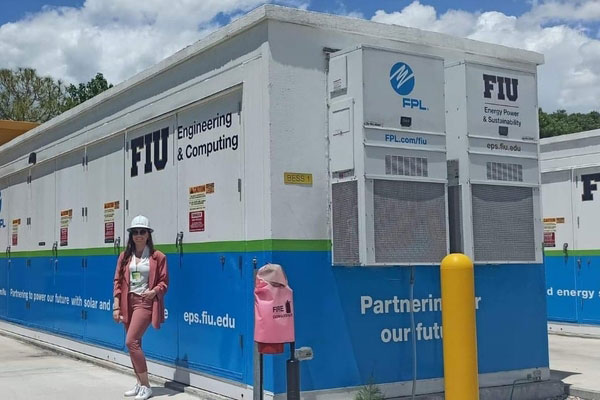 A picture of Ina Gjika standing in front of a large battery storage unit.