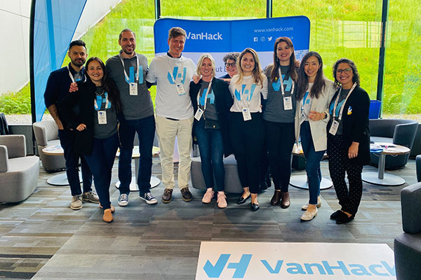 Ilya Brotzky standing and posing with 10 men and women, all smiling, in front of a window and with VanHack signage in the foreground and background.