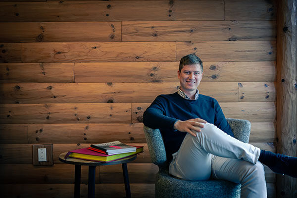 Ilya Brotzky sitting in a chair in front of a wood paneled wall.