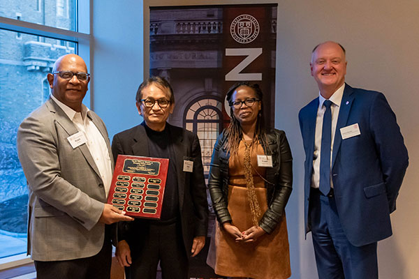 Four Cornell professors smiling at an event. One is female; the other three are men. One of the men is holding an award he has won.