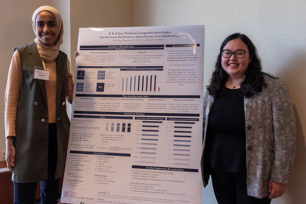 Two female graduate students standing next to a research poster.