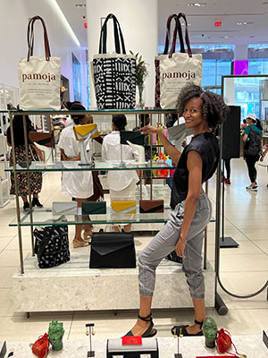 A young Black woman stands next to a display of handbags on glass shelves in a department store.