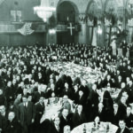 Black and white image of people in formal business attire in a grand banquet hall.