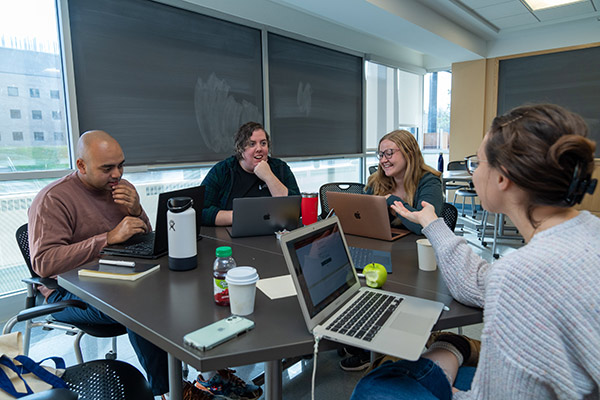 4 students, 1 male and 3 female, sitting at a table with laprops and discussing their ideas.