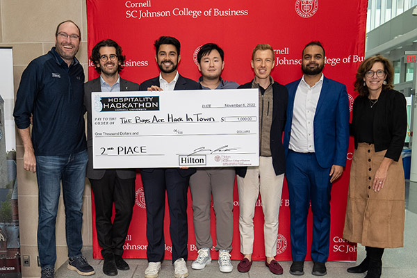 seven people standing in front of a red SC Johnson College of Business backdrop holding a large novelty check. 